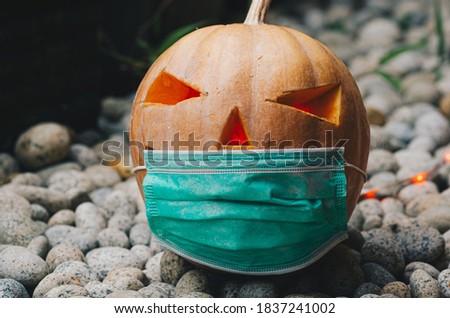 Close up view of Halloween pumpkin lantern wearing a medical facial mask as a symbol of disease control and virus infection and coronavirus or covid-19
