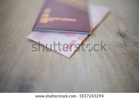 Picture of a One Hundred Thai Baht Bill Partially Inside a blurry Sweden Passport