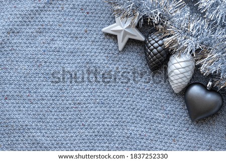 Gray knitted background with silver tinsel garland and Christmas tree toys: heart, star and pine cones