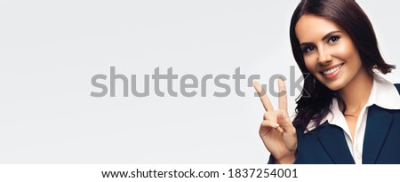 Happy smiling beautiful young businesswoman in blue confident suit, showing two fingers or victory gesture, isolated over grey background. Copy space for some ad text or imaginary.