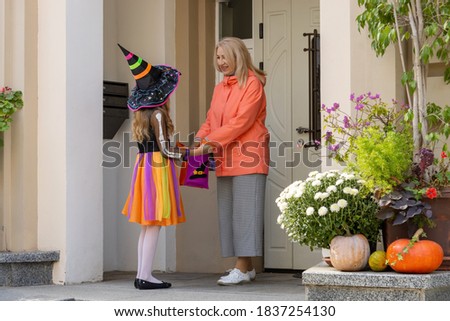 Little girl dressed in a witch costume asks an adult woman for candy at Halloween holiday.