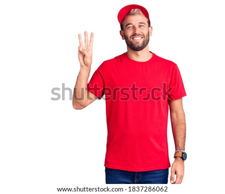 Young handsome blond man wearing t-shirt and cap showing and pointing up with fingers number three while smiling confident and happy. 