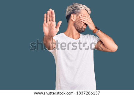 Young handsome blond man wearing casual t-shirt shouting with crazy expression doing rock symbol with hands up. music star. heavy concept. 