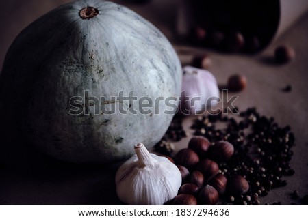 Blue pumpkin, Hazelnuts in nutshell, Fresh garlic bulbs with Mixed sorts and colors peppercorns on beige  background. Muted brightness image. Concept of autumnal harvest and organic vegetarian food.