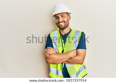 Handsome man with beard wearing safety helmet and reflective jacket happy face smiling with crossed arms looking at the camera. positive person.  Royalty-Free Stock Photo #1837297954