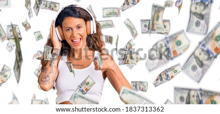 Young hispanic woman with tattoo listening to music using headphones smiling happy and positive, thumb up doing excellent and approval sign