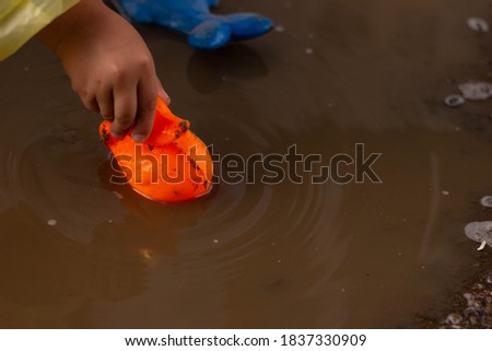 Beautiful girl in denim suit and yellow rubber boots plays with plastic duck and whale in a puddle