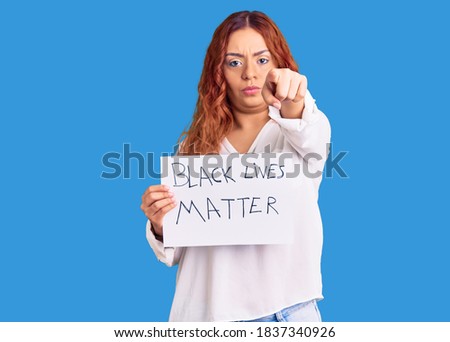 Young latin woman holding black lives matter banner pointing with finger to the camera and to you, confident gesture looking serious 