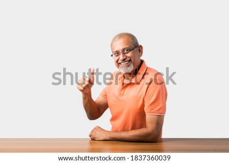 Portrait of Indian asian senior man sitting at table presenting or in success pose Royalty-Free Stock Photo #1837360039