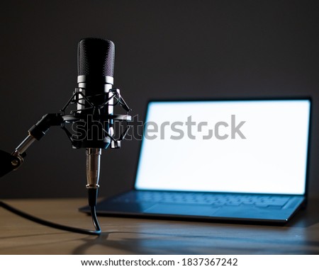 Professional microphone and laptop with white screen in the dark. Equipment in a recording and broadcasting studio