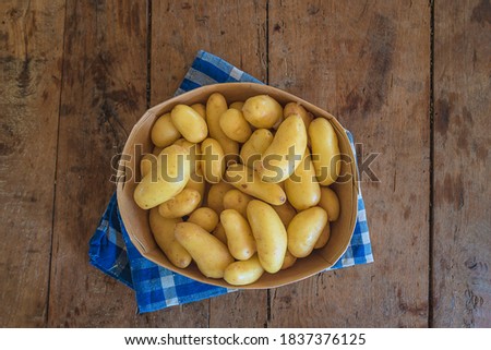 Basket with raw potatoes on checkered napkin and rustic wooden non paint background. Top view