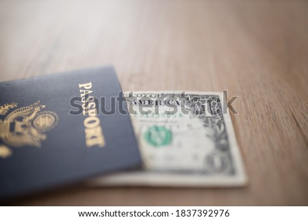 Picture of One-Dollar Bill Partially covered by a United States of America Passport on a Wooden Table
