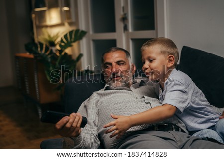 grandfather with his grandson sitting on sofa and watching television at home. evening scene
