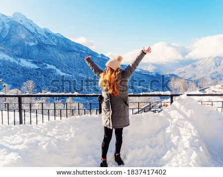 A joyful girl stands with her arms outstretched against the backdrop of snowy mountains