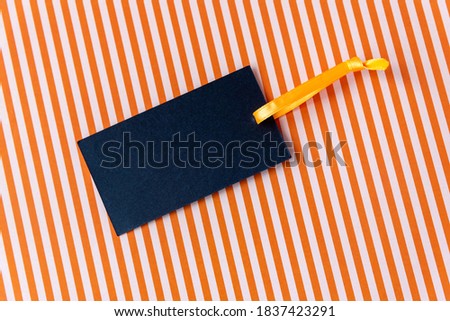 Blank paper card with space for design and yellow silk ribbon lying on bright color background with red and white stripes view from above. Black Friday concept