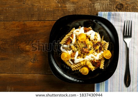Pasta with chicken and cheese in a black plate on a napkin with a fork.