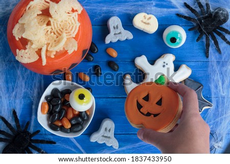 Top view of woman's hand holding halloween cookie with other treats on table