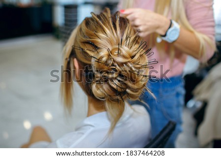 professional hairdresser braiding hair of young beautiful girl. Preparing for a party or holiday. A beautiful bride marries her husband. Lots of hair pins