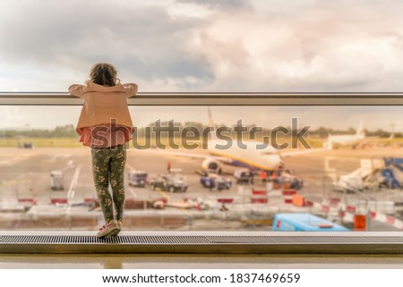 Silhouette of young girl on airport terminal. Standing on windowsill and looking on airplanes, waiting for departure. Dublin, Ireland