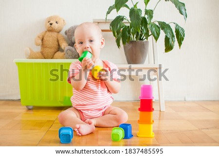 Little baby girl sitting on the floor, crawling and playing with brightly colored educational toys