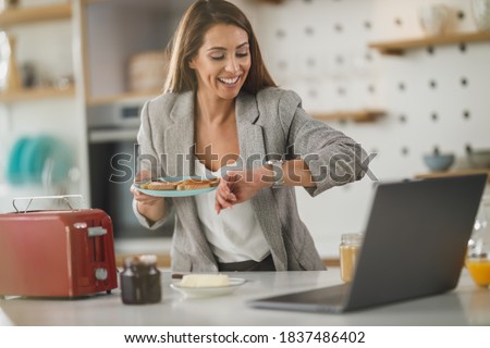 Shot of a multi-tasking young business woman having a breakfast and using laptop in her kitchen while getting ready to go to work. Royalty-Free Stock Photo #1837486402