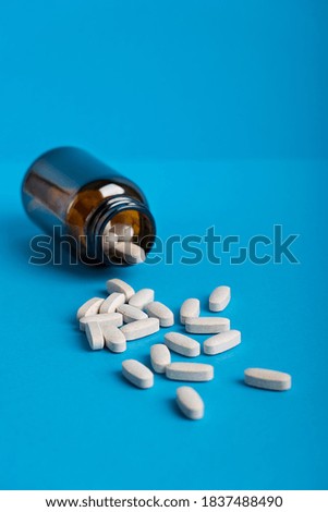 Image with selective focus of tablets or pills of dietary supplement or vitamins in brown glass bottle container against blue background aimed to prevent disease. Vertical orientation, modern concept