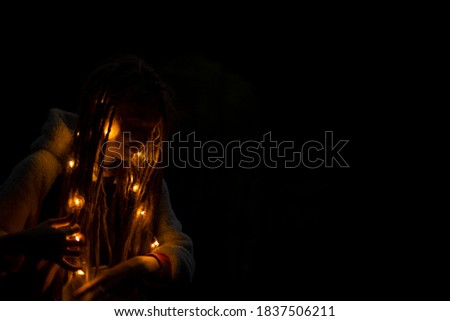 soft focus concept portrait of dreadlock girl in night darkness with garland lamps illumination in hair on black background empty copy space for your text here 