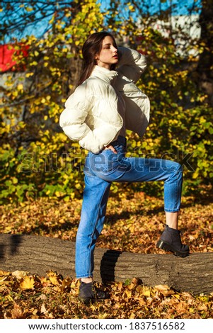 Full body portrait of a young beautiful brunette girl in blue jeans, autumn park outdoor