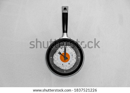 breakfast time concept fried egg on cooking pan shaped clock on light background