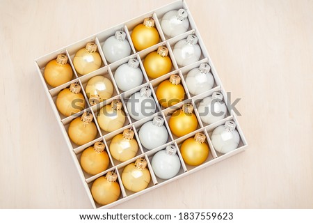 Christmas ornaments with golden and silver Xmas balls in a white box on an wooden background. Above view of Christmas balls.