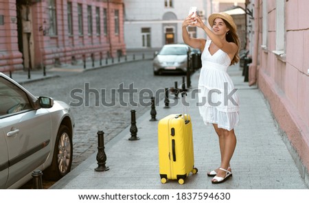 Woman traveler tourist walks with luggage in the city streets. take pictures of landmarks on your phone.