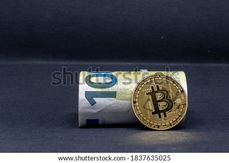 on a dark background lies a roll of euro banknotes and in front of it a golden Bitcoin coin