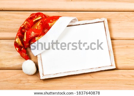 Christmas frame mockup for greeting card with Santa Claus hat on a wooden background. Christmas greeting card, banner. Winter holiday theme. Happy New Year. Copy space, flat lay.