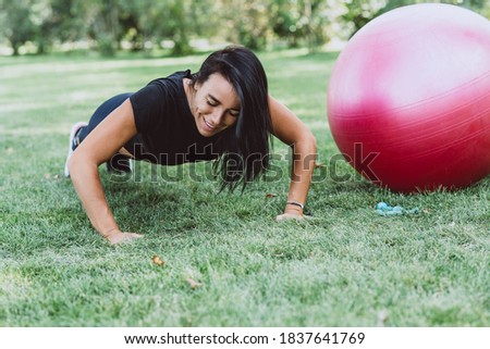 Young happy fit tanned brunette goes in for sports with a big fitness ball, dressed in active black clothes, does exercises, works out, posing in the park, walks outdoors. Soft selective focus.