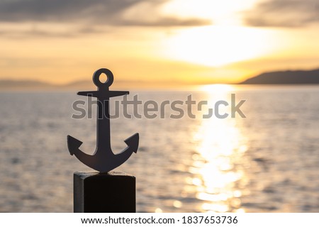 Silhouette of a stylized ship anchor on the pier on the background of the sunset. Sea voyage. Space for text.