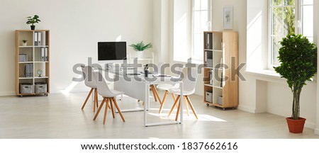 Interior of modern empty white business office room well-lit with daylight. Cozy spacious workspace with table, desktop computer and chairs for brainstorm meetings, online calls, staff training Royalty-Free Stock Photo #1837662616