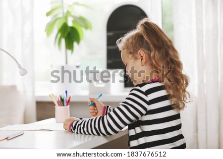 Charming girl draws a rainbow in an album. Side view, space for text. Home games, homework, home training, social distance