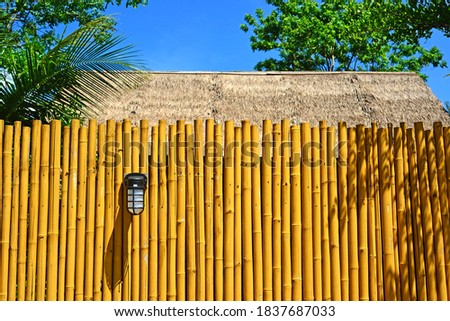  Outdoor Wall Lamp on bamboo fence with a straw roof behind.