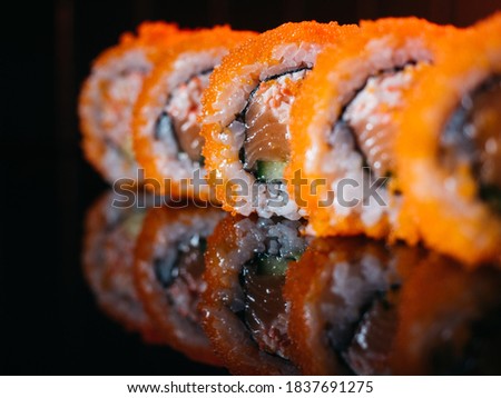 Sushi rolls with orange tobiko caviar, salmon and avocado snow crab served on reflective background