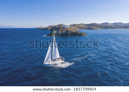 Sailing. Sailboat with white sails, rippled sea background, Lighthouse on a cape. Greece, Kea Tzia island. Summer holidays in Aegean sea. Aerial drone view Royalty-Free Stock Photo #1837709854