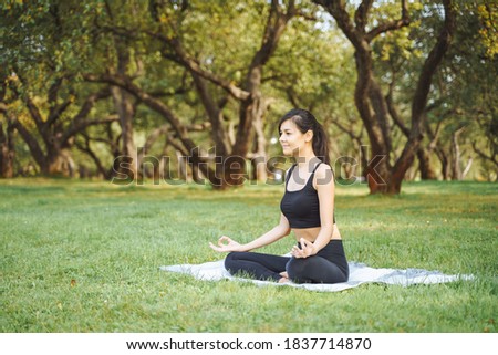Young attractive woman meditating in lotus position sitting on the grass in the park. Yoga and harmony concept.