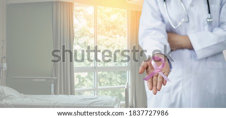 Pink ribbon in doctor's hand in patient room Healthcare, medicine and breast cancer concept.