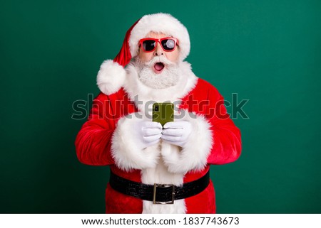 Photo of pensioner stylish grandpa grey hair beard hold telephone shocked open mouth crazy novelty wear red santa x-mas costume coat gloves sunglass headwear isolated green color background