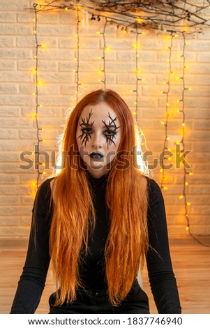 Halloween ginger Witch woman with long hair and fashion halloween make up. Garland and natural panel of branches and dried flowers on background.