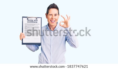 Young woman with short hair holding clipboard with terms and conditions document doing ok sign with fingers, smiling friendly gesturing excellent symbol 