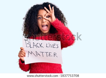 African american child with curly hair holding black lives matter banner smiling happy doing ok sign with hand on eye looking through fingers 