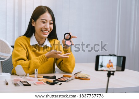 Beautiful asian woman blogger using camera phone recording vlog video live streaming and showing how to make up cosmetics at home.