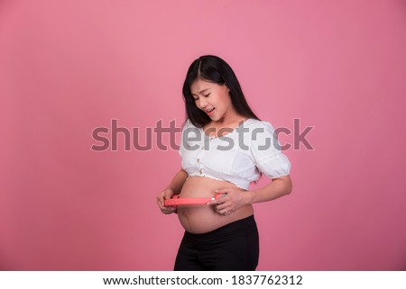 Beautiful pregnant Asian woman listening to music from
Headphones comfortably On a pink background , Expectation of young mothers, pregnancy pictures and childbirth