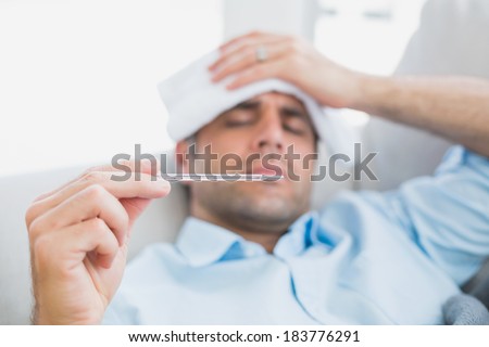 Sick man lying on sofa checking his temperature at home in the living room Royalty-Free Stock Photo #183776291