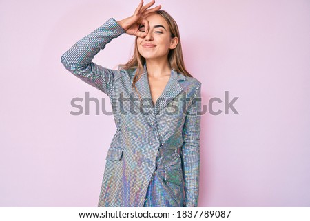 Young beautiful blonde woman wearing business jacket smiling happy doing ok sign with hand on eye looking through fingers 